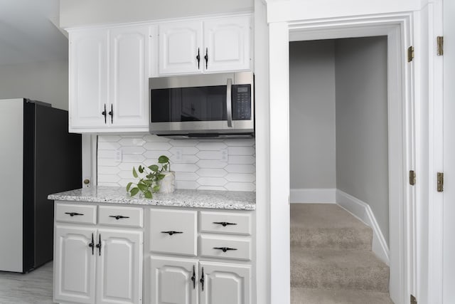 kitchen with light stone countertops, tasteful backsplash, black refrigerator, white cabinets, and light wood-type flooring