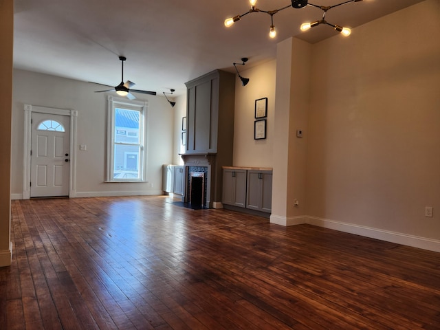 unfurnished living room with ceiling fan with notable chandelier and dark wood-type flooring