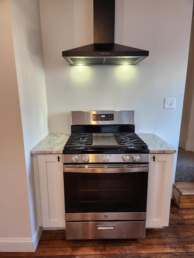 kitchen featuring light stone counters, wall chimney exhaust hood, gas range, dark hardwood / wood-style floors, and white cabinetry