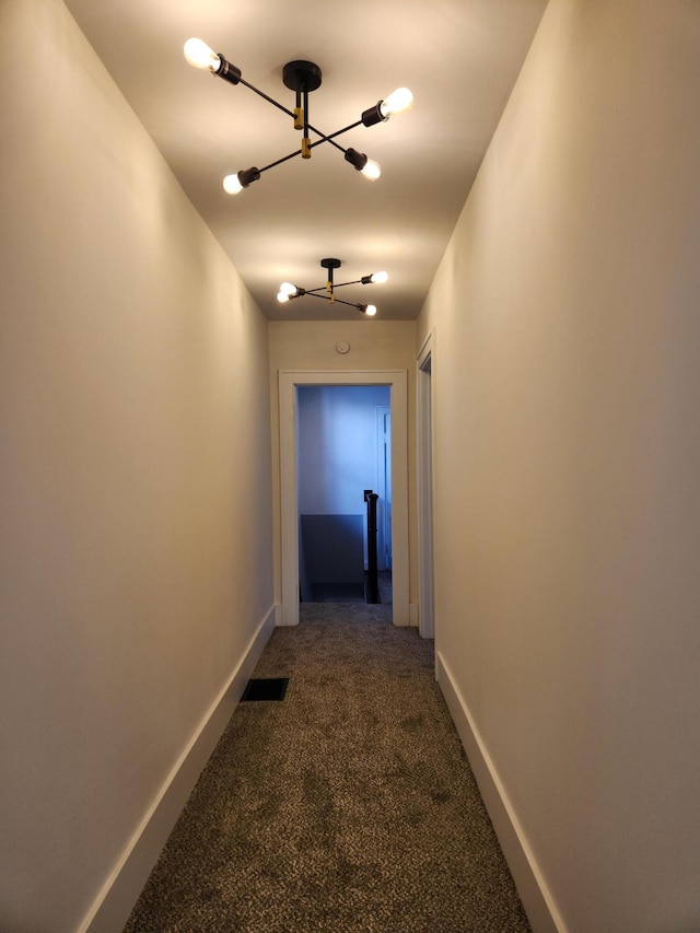 hallway featuring dark colored carpet and an inviting chandelier