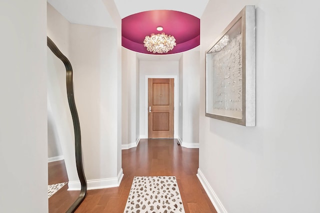 hallway featuring hardwood / wood-style flooring, a tray ceiling, and an inviting chandelier