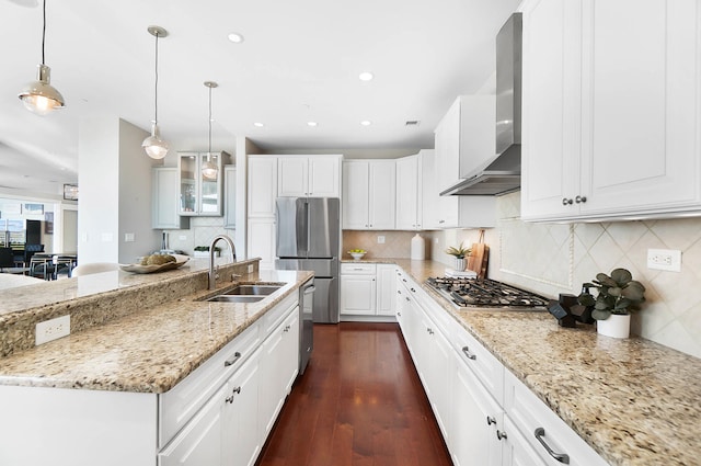 kitchen with pendant lighting, white cabinets, wall chimney range hood, stainless steel appliances, and sink