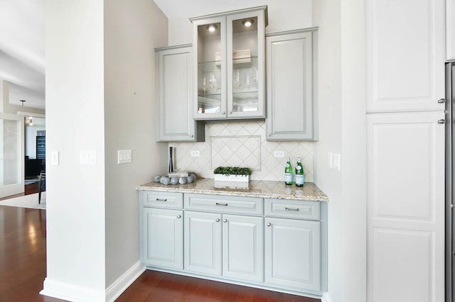 bar featuring tasteful backsplash, dark hardwood / wood-style flooring, light stone counters, and gray cabinets