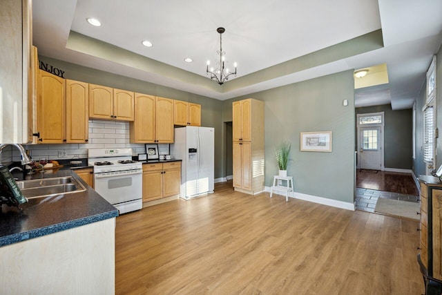 kitchen with sink, a raised ceiling, pendant lighting, white appliances, and light hardwood / wood-style floors