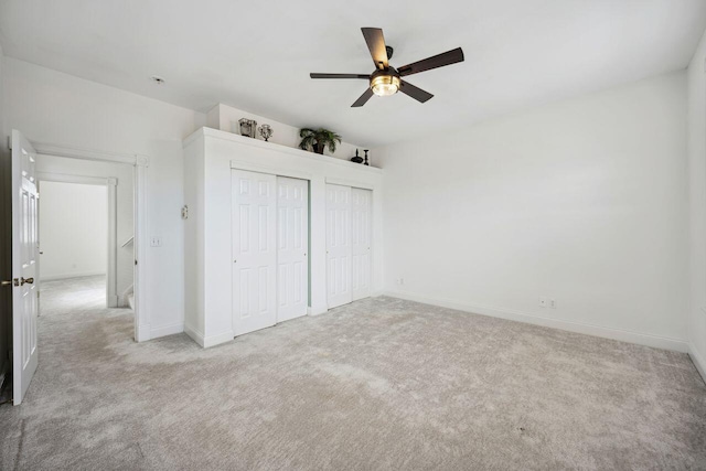 unfurnished bedroom with light carpet, two closets, and ceiling fan