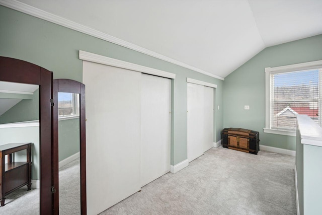 unfurnished bedroom featuring lofted ceiling, light carpet, and multiple closets