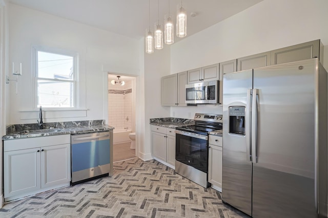 kitchen with sink, hanging light fixtures, dark stone counters, gray cabinets, and appliances with stainless steel finishes