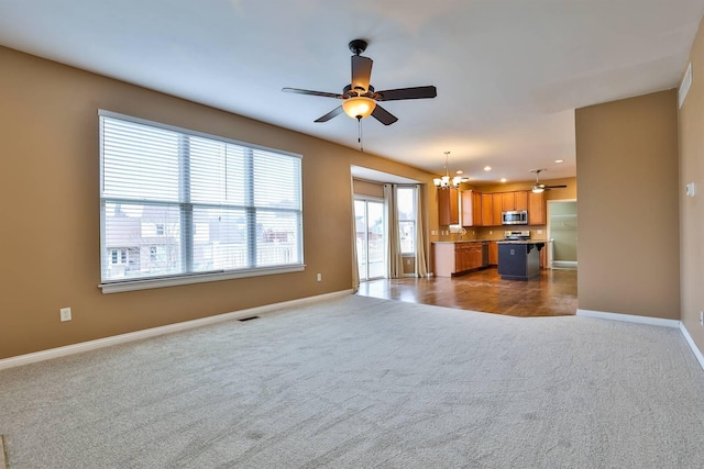 unfurnished living room with ceiling fan with notable chandelier and dark colored carpet