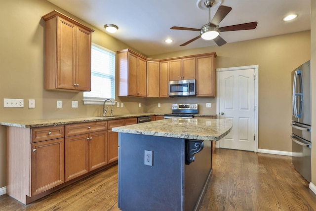 kitchen featuring a center island, sink, stainless steel appliances, light stone counters, and hardwood / wood-style flooring