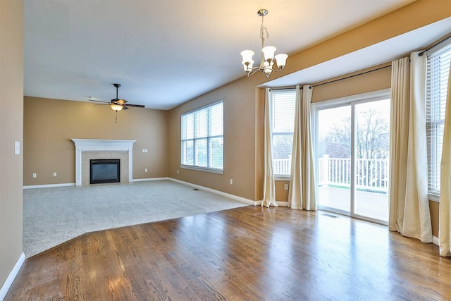 unfurnished living room with ceiling fan with notable chandelier, hardwood / wood-style flooring, and a tiled fireplace