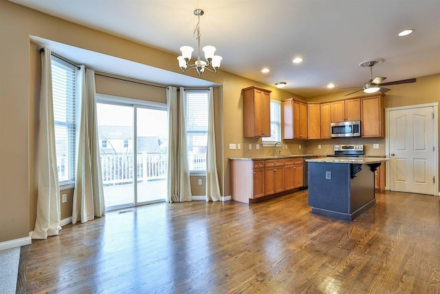 kitchen with appliances with stainless steel finishes, dark hardwood / wood-style flooring, ceiling fan with notable chandelier, sink, and a center island