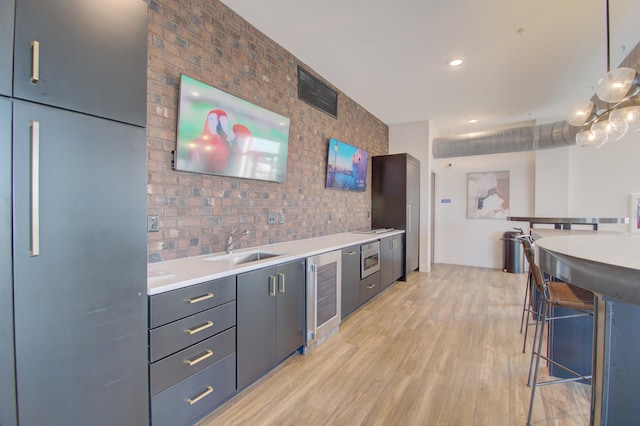 kitchen featuring light wood-type flooring, a breakfast bar, beverage cooler, sink, and decorative light fixtures