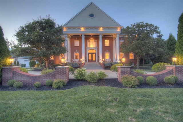 neoclassical home with a front yard, a porch, french doors, and brick siding