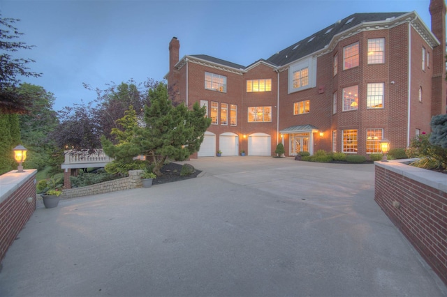 view of front of property featuring an attached garage, brick siding, driveway, and a chimney