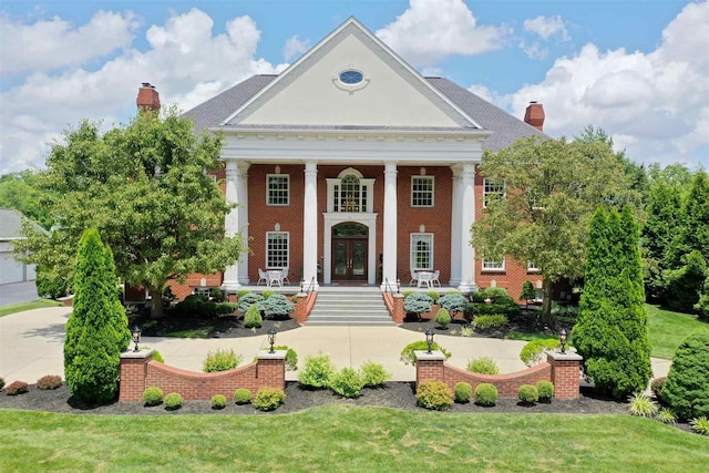 neoclassical home with brick siding, covered porch, french doors, and a chimney