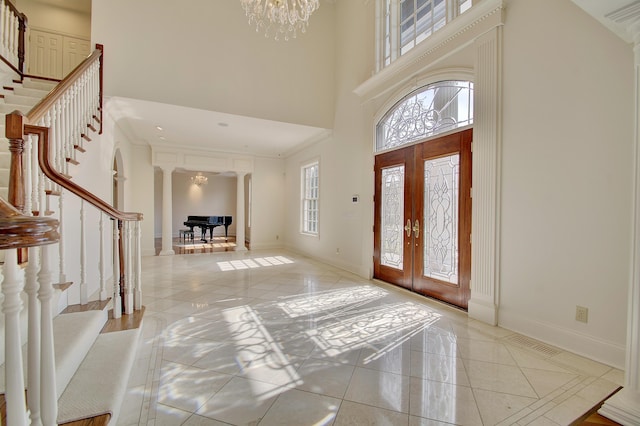 entryway featuring baseboards, a high ceiling, an inviting chandelier, and ornate columns