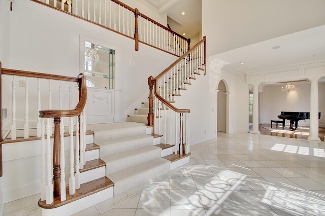 tiled foyer entrance featuring stairway, a high ceiling, decorative columns, arched walkways, and crown molding