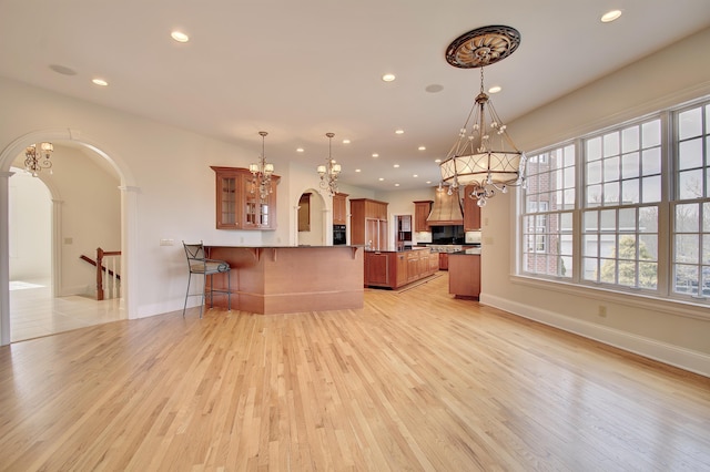 kitchen with a peninsula, arched walkways, light wood-style floors, a kitchen bar, and brown cabinets