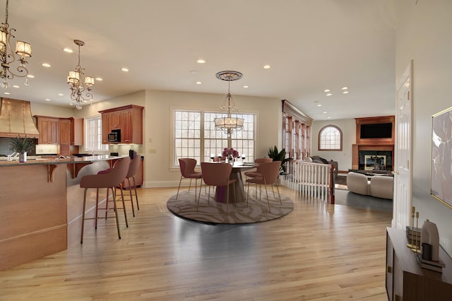 dining space with a glass covered fireplace, a notable chandelier, recessed lighting, and light wood finished floors