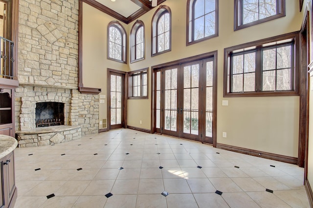 unfurnished living room with a stone fireplace, plenty of natural light, french doors, and baseboards