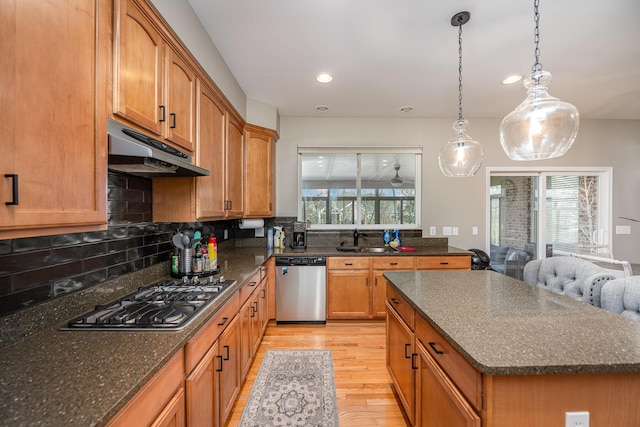 kitchen with appliances with stainless steel finishes, sink, decorative backsplash, hanging light fixtures, and light hardwood / wood-style floors