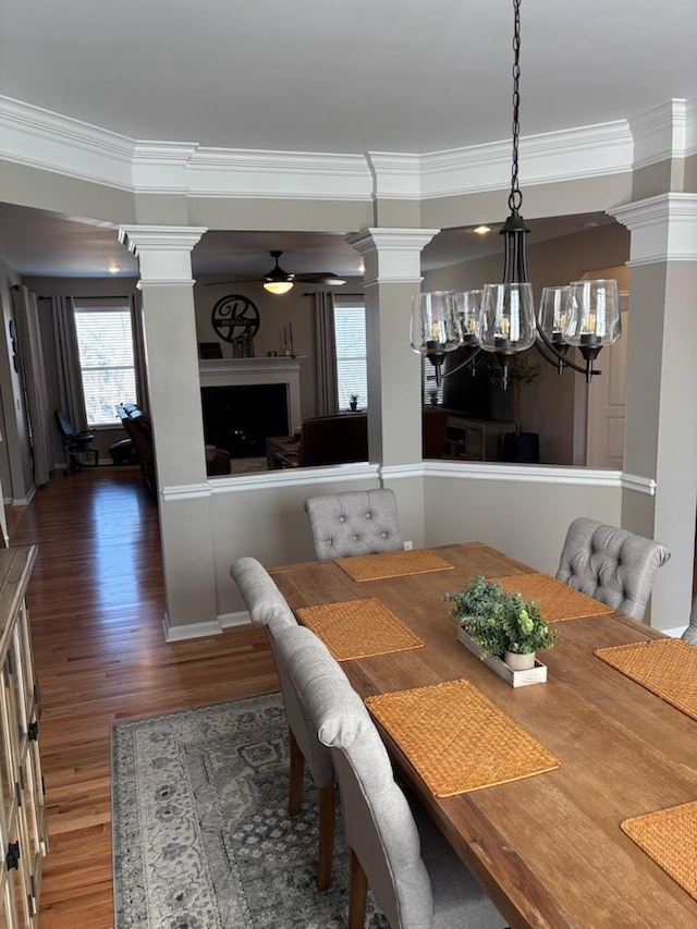 dining space featuring crown molding, dark wood-type flooring, decorative columns, and ceiling fan