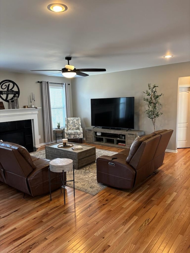 living room featuring ceiling fan, a tile fireplace, and light wood-type flooring