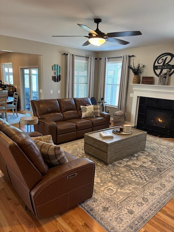 living room with a tile fireplace, wood-type flooring, and ceiling fan