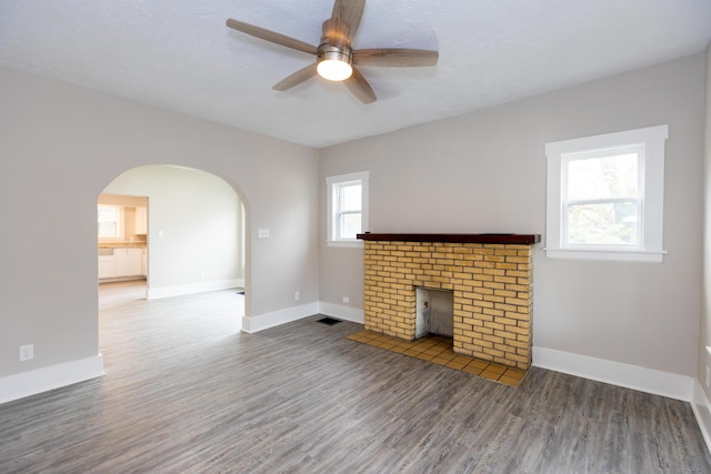 unfurnished living room with a textured ceiling, hardwood / wood-style flooring, a brick fireplace, and ceiling fan