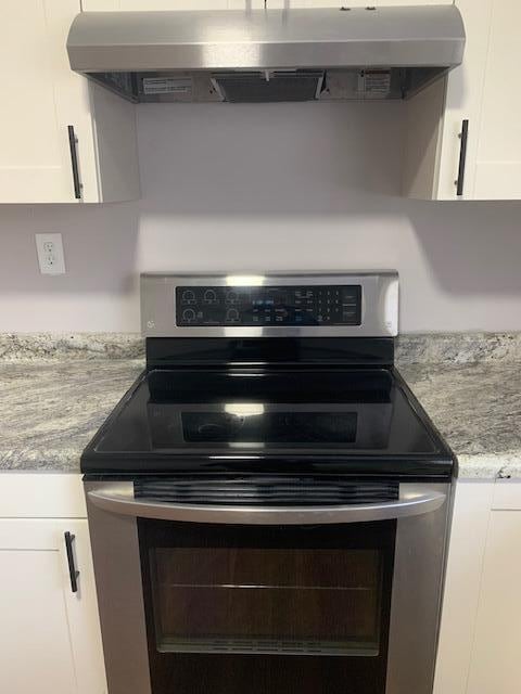 details with white cabinetry, range hood, light stone counters, and stainless steel range with electric stovetop