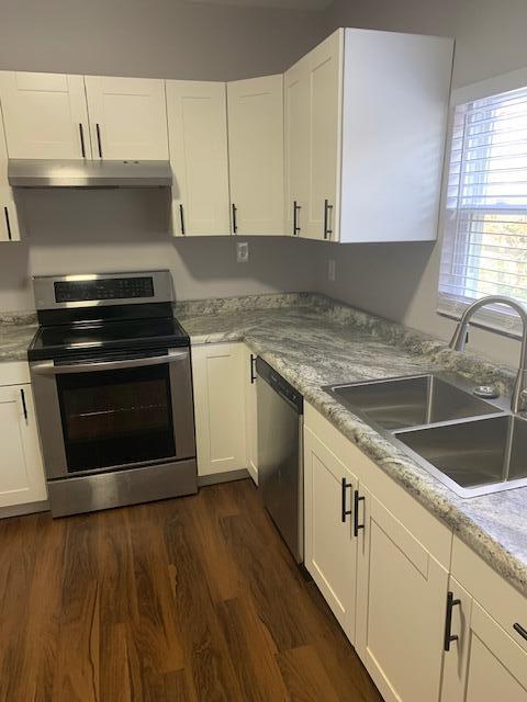 kitchen with light stone counters, stainless steel appliances, dark wood-type flooring, sink, and white cabinetry