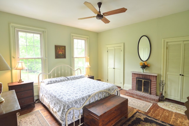 bedroom featuring a fireplace, hardwood / wood-style flooring, baseboard heating, and ceiling fan