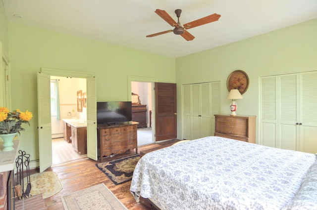 bedroom with ensuite bathroom, ceiling fan, a baseboard radiator, light hardwood / wood-style floors, and multiple closets