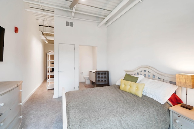 unfurnished bedroom featuring carpet floors, ensuite bath, beamed ceiling, and a high ceiling