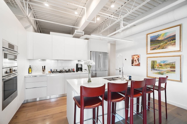 kitchen with stainless steel appliances, hardwood / wood-style floors, a kitchen bar, a kitchen island with sink, and white cabinets