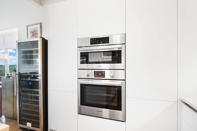 kitchen featuring wine cooler, white cabinetry, stainless steel double oven, and wood-type flooring