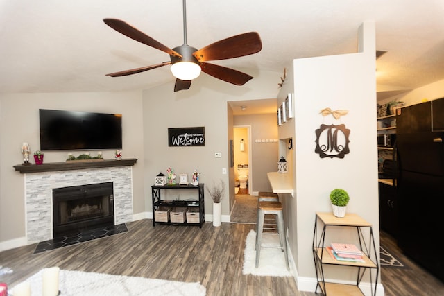 living room featuring dark hardwood / wood-style flooring, a stone fireplace, ceiling fan, and lofted ceiling