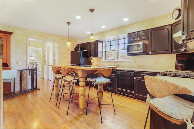 kitchen with dark brown cabinetry, light hardwood / wood-style flooring, black appliances, and a breakfast bar