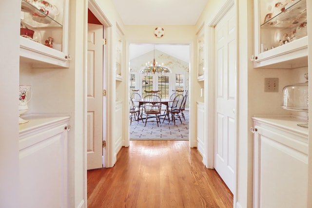 hallway featuring a notable chandelier, vaulted ceiling, and light hardwood / wood-style floors