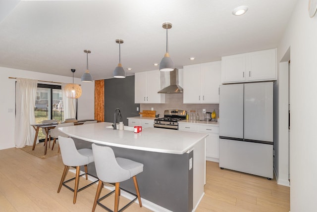 kitchen featuring a center island with sink, white refrigerator, gas range, wall chimney exhaust hood, and white cabinetry