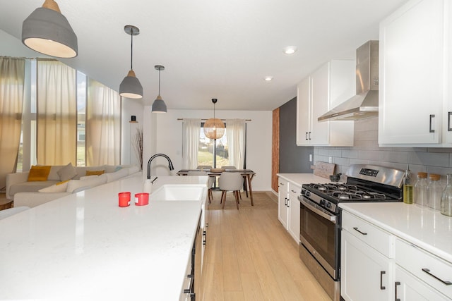 kitchen featuring gas range, sink, wall chimney range hood, light hardwood / wood-style flooring, and hanging light fixtures