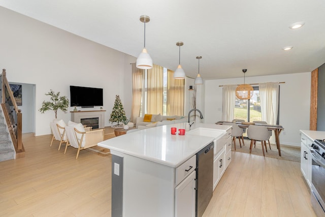 kitchen with pendant lighting, a kitchen island with sink, white cabinets, light wood-type flooring, and stainless steel appliances