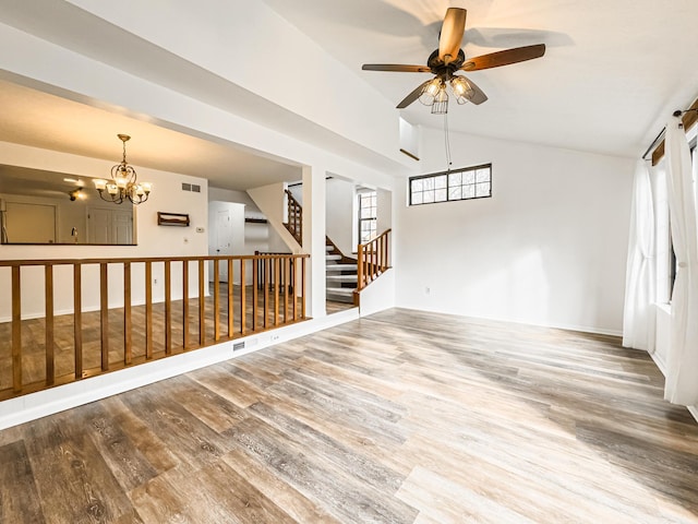 empty room featuring wood-type flooring, ceiling fan with notable chandelier, and vaulted ceiling