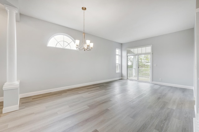 spare room with a chandelier, decorative columns, and light hardwood / wood-style flooring