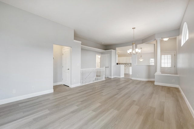 unfurnished living room with light hardwood / wood-style floors, decorative columns, and a chandelier