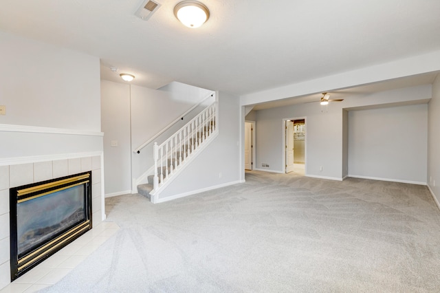 unfurnished living room with a tiled fireplace, ceiling fan, and light colored carpet