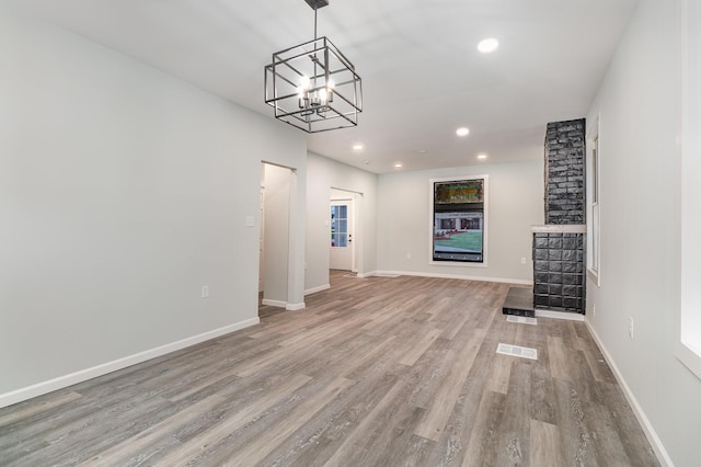 unfurnished living room with light hardwood / wood-style floors, a fireplace, and an inviting chandelier