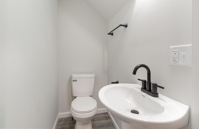 bathroom with toilet, hardwood / wood-style floors, vaulted ceiling, and sink