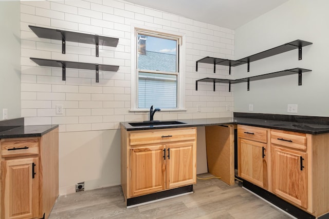 kitchen with backsplash, light wood-type flooring, sink, and dark stone counters