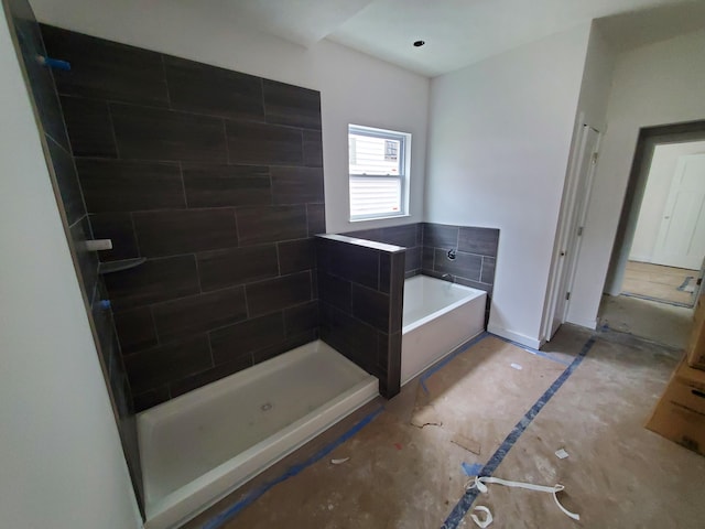 bathroom with a garden tub, a tile shower, and baseboards